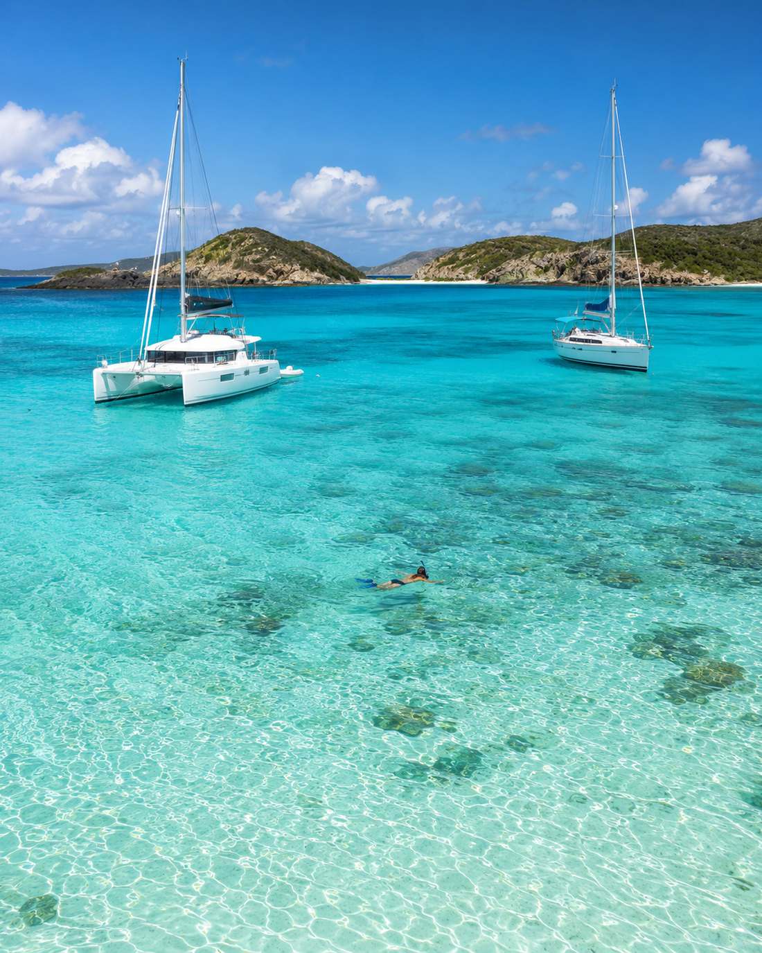 Two sailboats anchored on a shallow turquoise reef in the Virgin Islands